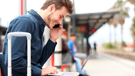 Un hombre en una plataforma de tren participa en un webinar gratuito desde una laptop y app móvil