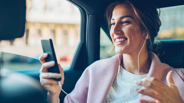 Nainen autossa hymyilee käyttäessään puhelintaan