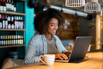 Femme souriant dans un café en train d'utiliser un partage d'écran pour collaborer depuis son ordinateur portable