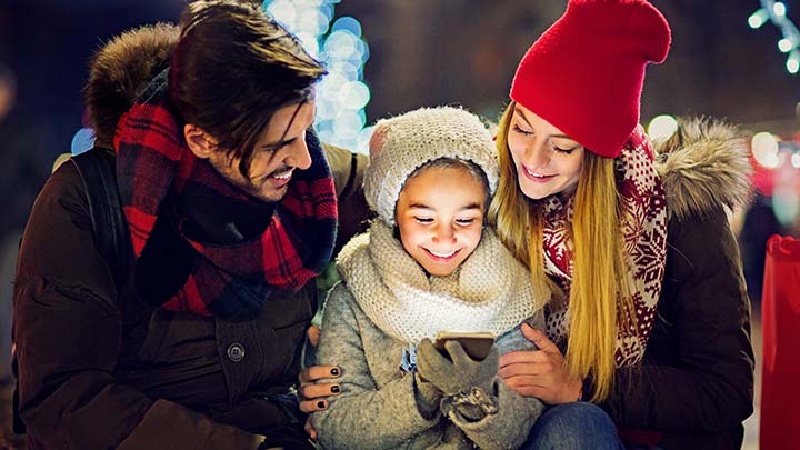 Con luces de Navidad en el fondo, una pequeña familia camina afuera en invierno y deja un mensaje en la Línea Telefónica de Santa