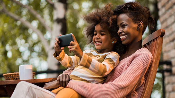 Madre e figlio suduti all'aperto in un clima caldo con un telefono cellulare in vivavoce, che ascoltano la Hotline di Babbo Natale