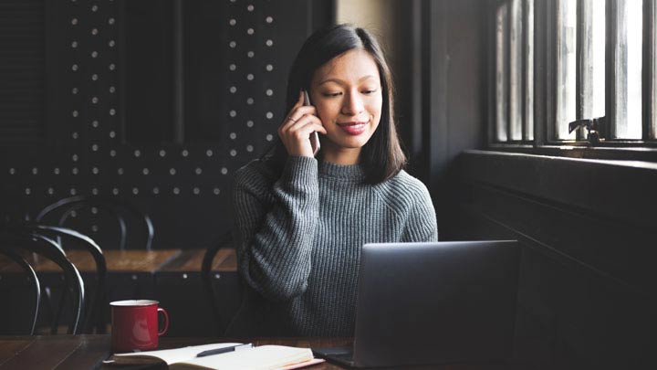 Sitzende Frau am Telefon mit Laptop